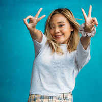 Smiling female student with both arms raised and hands making peace signs